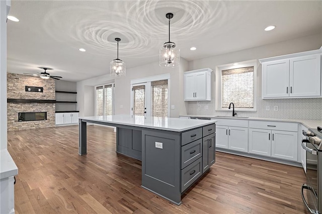 kitchen featuring gray cabinetry, a sink, wood finished floors, white cabinetry, and a stone fireplace