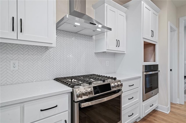 kitchen with stainless steel appliances, light countertops, white cabinetry, wall chimney exhaust hood, and tasteful backsplash