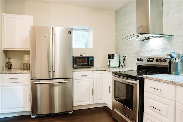 kitchen with white cabinetry, stainless steel appliances, light stone counters, decorative backsplash, and wall chimney range hood