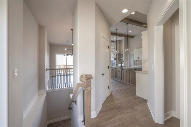 hall featuring baseboards, beamed ceiling, light wood-style floors, a sink, and recessed lighting