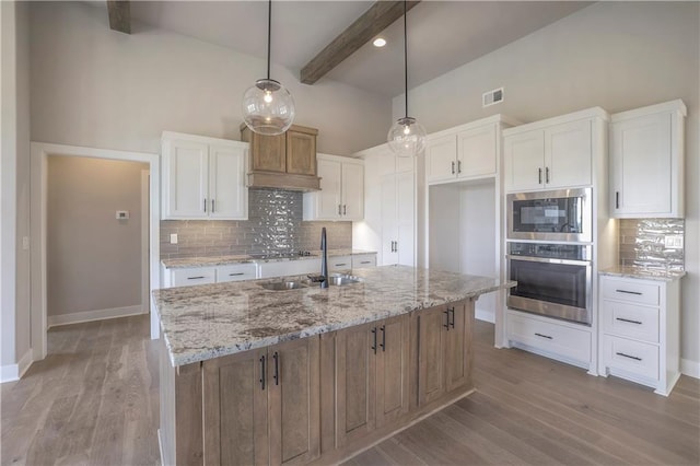 kitchen featuring light wood finished floors, visible vents, white cabinets, beamed ceiling, and a sink