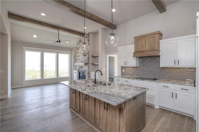 kitchen featuring light wood-style floors, white cabinets, a sink, and a stone fireplace