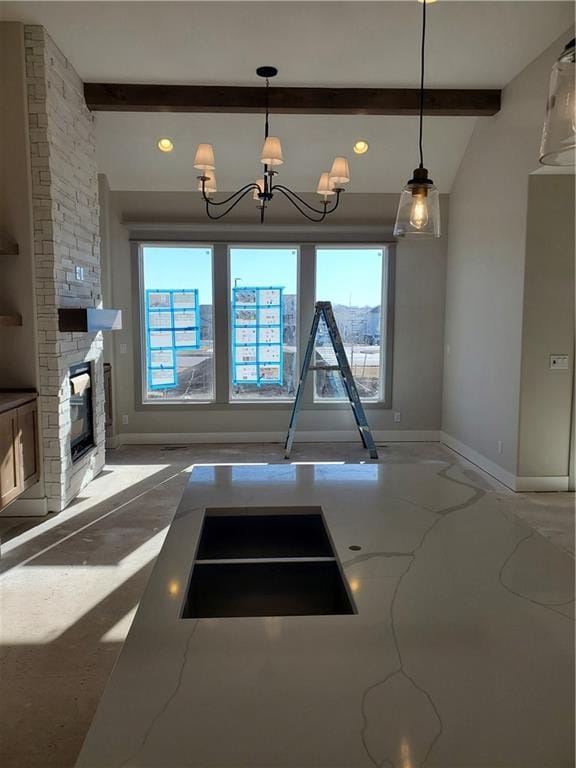 interior space with a stone fireplace, baseboards, light stone countertops, beamed ceiling, and plenty of natural light