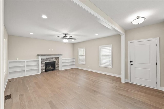 unfurnished living room with ceiling fan, a stone fireplace, and light hardwood / wood-style flooring