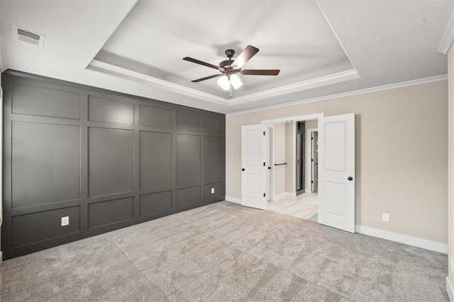 unfurnished bedroom featuring a raised ceiling, ornamental molding, light carpet, and ceiling fan