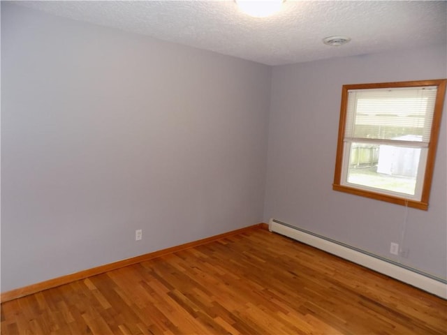 empty room with wood-type flooring, a textured ceiling, and baseboard heating