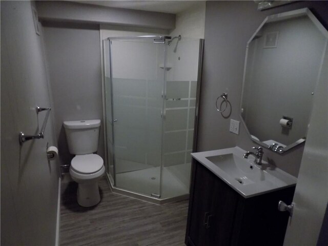 bathroom with hardwood / wood-style floors, a shower with door, toilet, and vanity