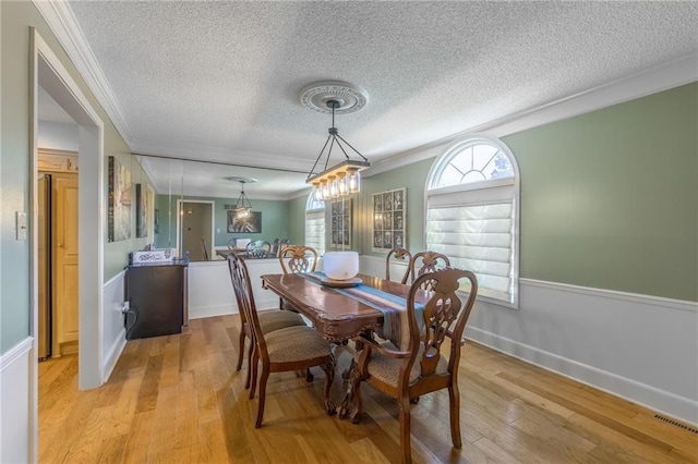 dining space with light hardwood / wood-style floors, crown molding, and a textured ceiling