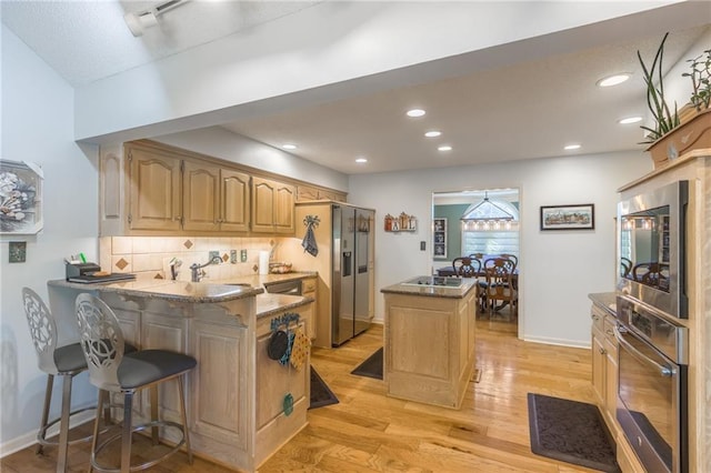 kitchen featuring a kitchen bar, appliances with stainless steel finishes, kitchen peninsula, and light wood-type flooring