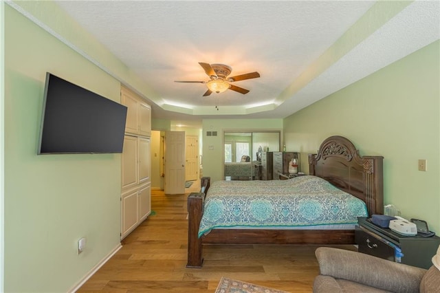 bedroom with a raised ceiling, light wood-type flooring, and ceiling fan