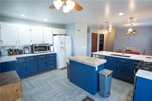 kitchen with white cabinets, hanging light fixtures, a kitchen island, appliances with stainless steel finishes, and ceiling fan with notable chandelier