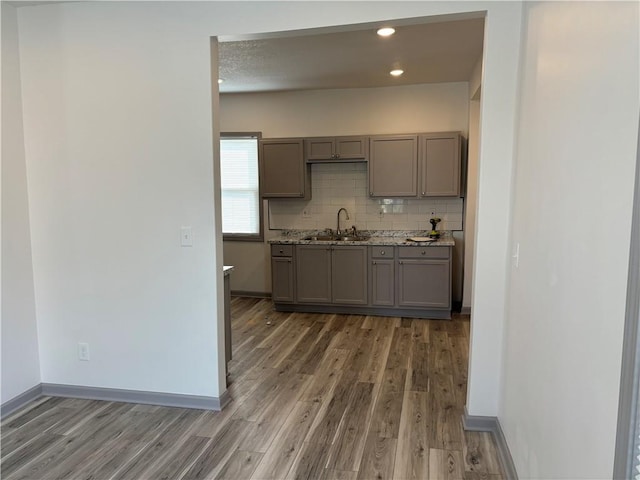 kitchen featuring gray cabinets, tasteful backsplash, wood-type flooring, sink, and light stone countertops