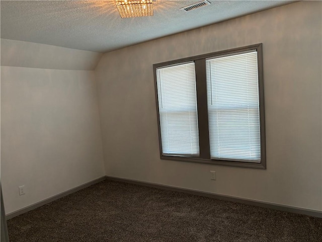 spare room with dark colored carpet, a textured ceiling, and vaulted ceiling