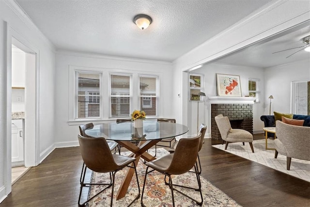 dining area with dark wood-type flooring, a fireplace, a textured ceiling, ceiling fan, and ornamental molding