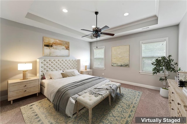 bedroom with ceiling fan, dark colored carpet, multiple windows, and a tray ceiling