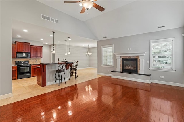 living room with a tiled fireplace, ceiling fan with notable chandelier, plenty of natural light, and light hardwood / wood-style floors