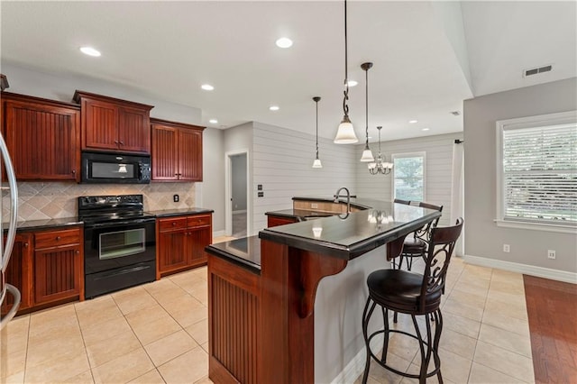 kitchen featuring light wood-type flooring, decorative light fixtures, black appliances, a kitchen bar, and a kitchen island with sink