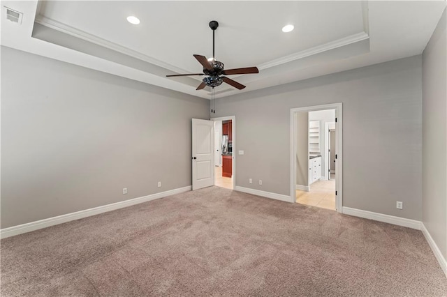 empty room featuring a tray ceiling, light carpet, crown molding, and ceiling fan