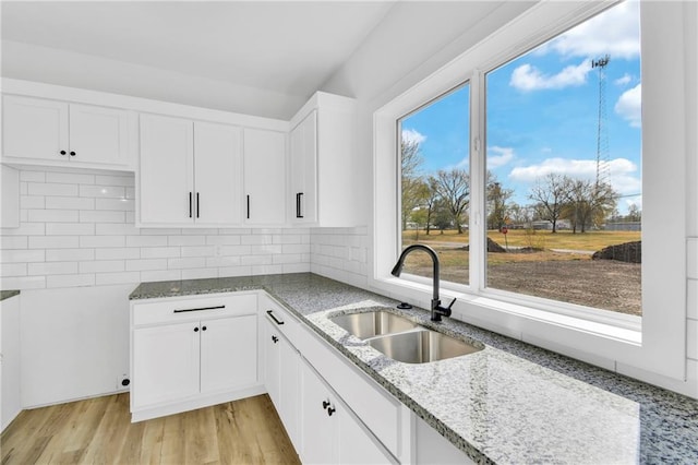 kitchen featuring light stone countertops, sink, light wood-type flooring, backsplash, and white cabinets