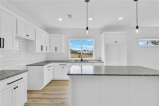 kitchen featuring light hardwood / wood-style flooring, dark stone counters, a center island, pendant lighting, and white cabinets