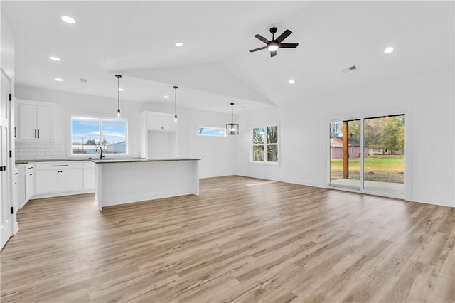 unfurnished living room featuring light hardwood / wood-style floors, high vaulted ceiling, sink, and ceiling fan with notable chandelier