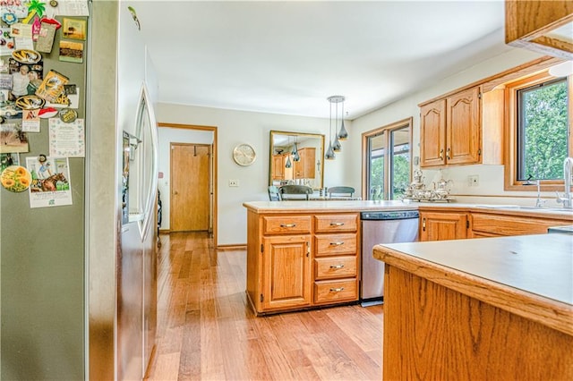 kitchen with kitchen peninsula, appliances with stainless steel finishes, decorative light fixtures, sink, and light wood-type flooring