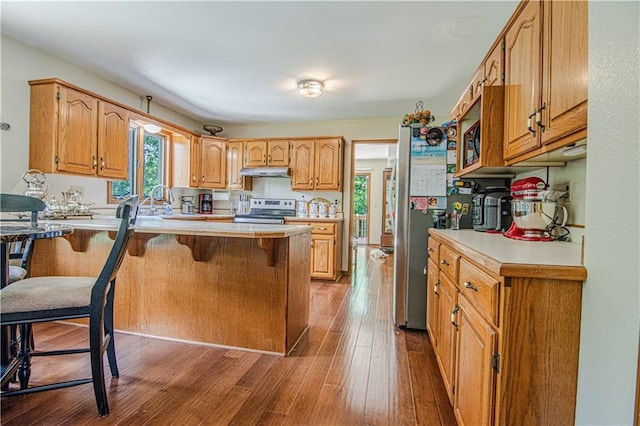 kitchen with kitchen peninsula, wood-type flooring, appliances with stainless steel finishes, sink, and a breakfast bar area