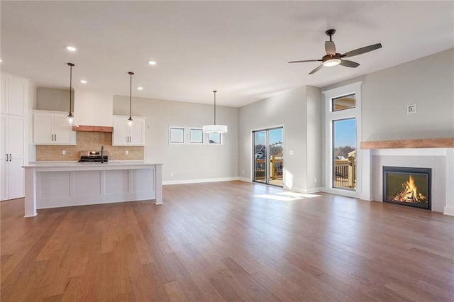 unfurnished living room with a tile fireplace, ceiling fan, sink, and light wood-type flooring