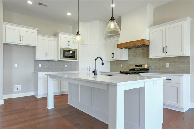 kitchen featuring built in microwave, white cabinetry, stainless steel range, pendant lighting, and a kitchen island with sink