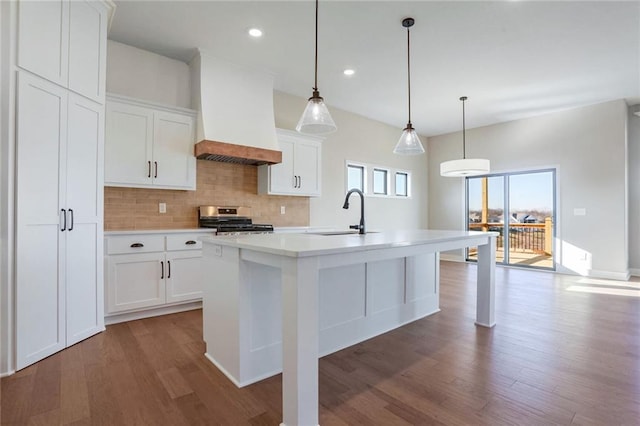 kitchen with pendant lighting, premium range hood, a kitchen island with sink, white cabinets, and sink