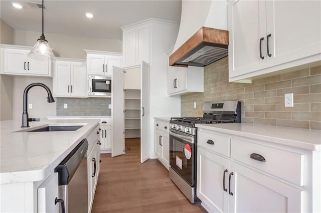 kitchen with hanging light fixtures, sink, custom range hood, appliances with stainless steel finishes, and white cabinetry