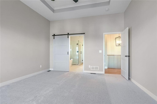 unfurnished bedroom with a raised ceiling, ensuite bath, ceiling fan, a barn door, and light colored carpet