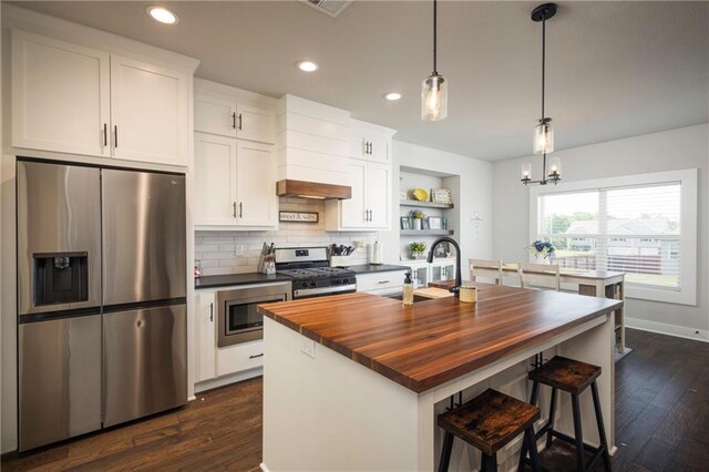 kitchen featuring dark wood-type flooring, stainless steel appliances, white cabinets, and a kitchen island with sink