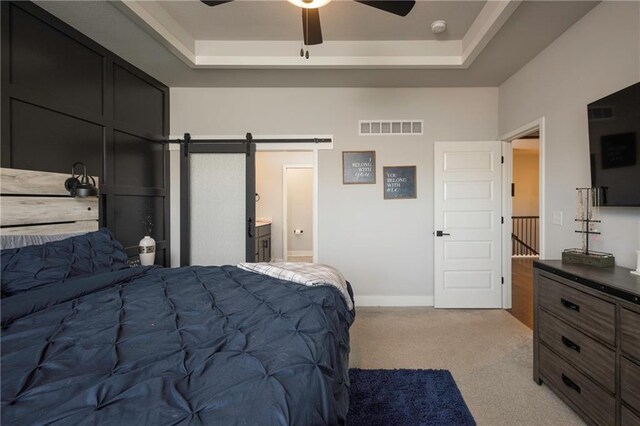 bedroom with light carpet, a tray ceiling, connected bathroom, a barn door, and ceiling fan