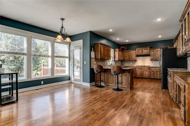 kitchen with a breakfast bar, hanging light fixtures, decorative backsplash, an inviting chandelier, and dark hardwood / wood-style flooring