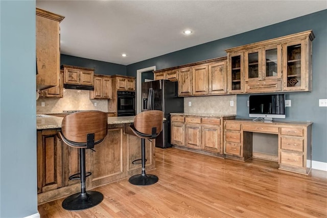 kitchen featuring a kitchen breakfast bar, black appliances, light hardwood / wood-style floors, and light stone counters