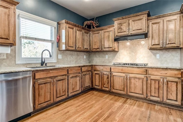 kitchen featuring light stone counters, sink, backsplash, stainless steel appliances, and light wood-type flooring