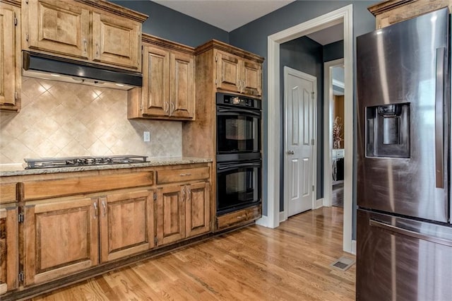 kitchen with light stone counters, light hardwood / wood-style floors, appliances with stainless steel finishes, and backsplash