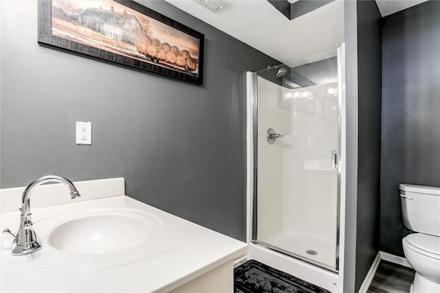 bathroom with a textured ceiling, hardwood / wood-style flooring, walk in shower, vanity, and toilet