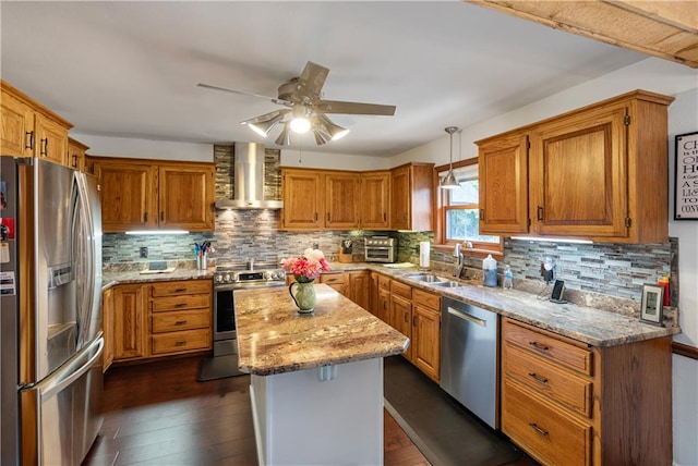 kitchen with decorative light fixtures, stainless steel appliances, a kitchen island, ceiling fan, and wall chimney range hood