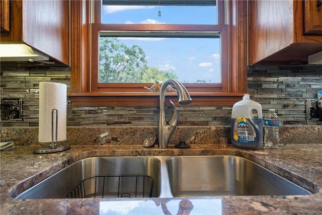 details featuring backsplash, dark stone counters, and sink