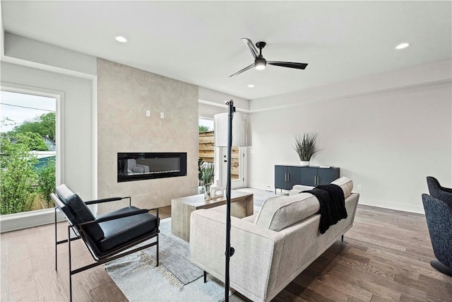 living room with wood-type flooring, a large fireplace, and ceiling fan