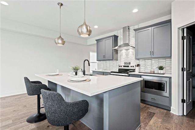 kitchen with sink, hanging light fixtures, wall chimney exhaust hood, a center island with sink, and appliances with stainless steel finishes