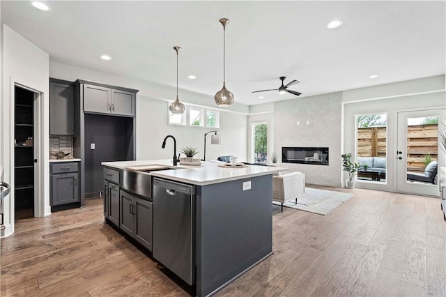 kitchen with ceiling fan, sink, stainless steel dishwasher, a center island with sink, and a large fireplace