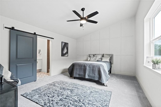 bedroom featuring vaulted ceiling, a barn door, light carpet, ensuite bath, and ceiling fan