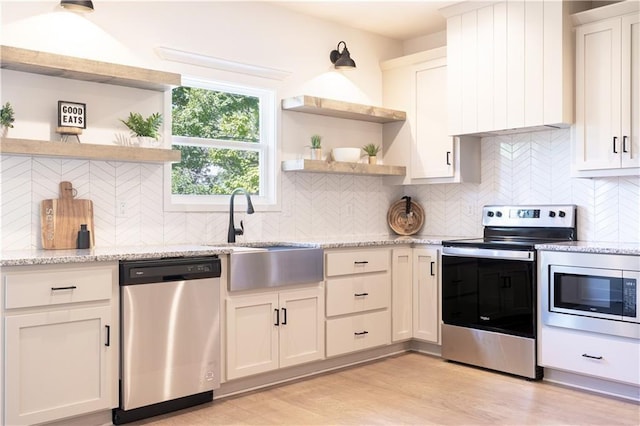 kitchen with appliances with stainless steel finishes, light wood-type flooring, light stone countertops, and white cabinets