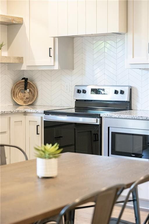 kitchen featuring decorative backsplash, stainless steel range with electric stovetop, light stone counters, and white cabinets