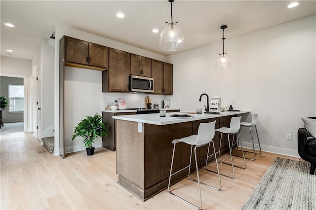 kitchen featuring pendant lighting, dark brown cabinets, light wood-type flooring, and kitchen peninsula