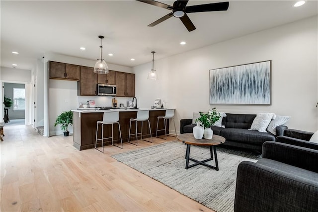 living room with light wood-type flooring, ceiling fan, and sink