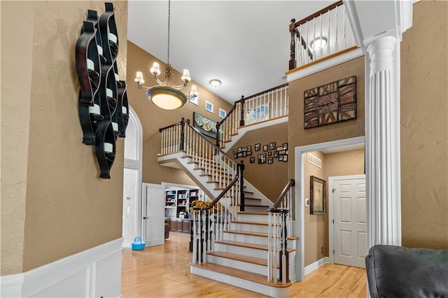 staircase with ornate columns, hardwood / wood-style flooring, an inviting chandelier, and a towering ceiling